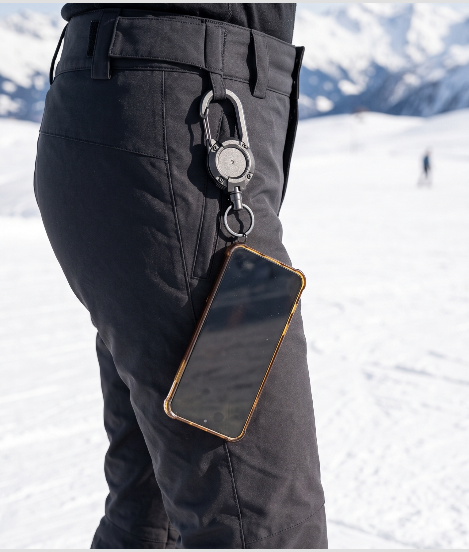 Telefoon hangt aan een uitrolbaar koord aan een zwarte skibroek op een besneeuwde piste
